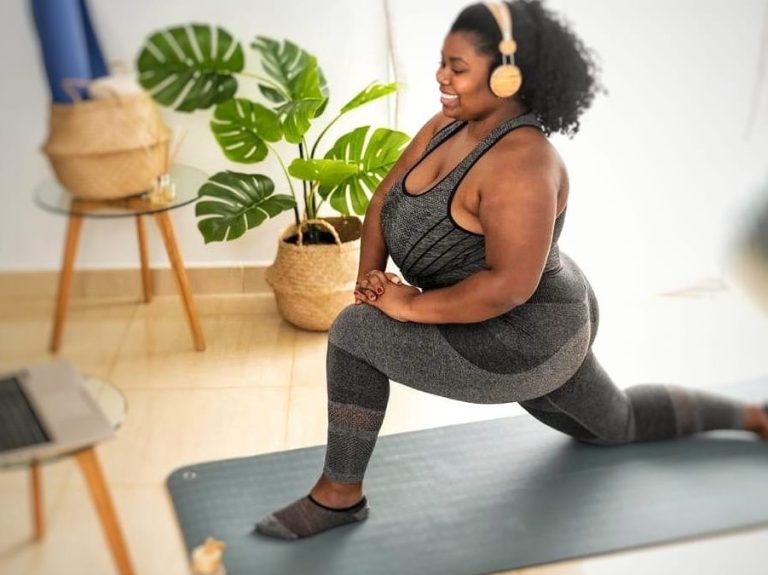 "Woman in her living room, following a programme or online coaching session on her laptop. Calm home setting, showing real-life balance"